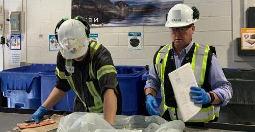 Two people in hard hats and vests sorting in a facility.